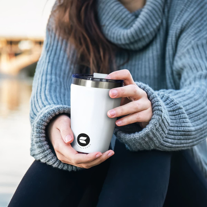 A drink bottle featuring a white exterior with a black logo, being held by a person in a grey sweater.