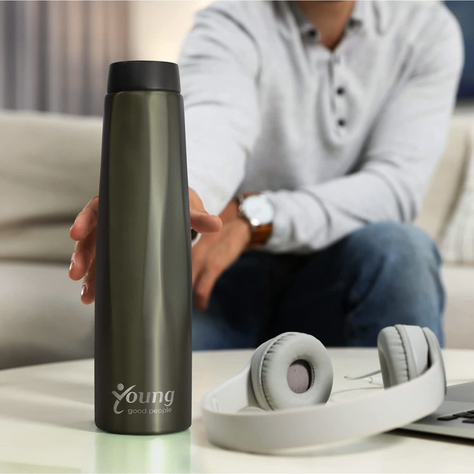 A drink bottle in a sleek, dark green colour with a logo, placed on a table beside headphones.