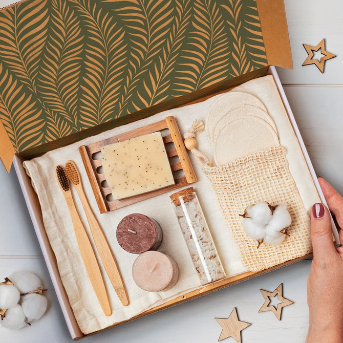 A die cut box with a locking lid, containing bamboo utensils, soap, candles, cotton balls, and a woven pouch.