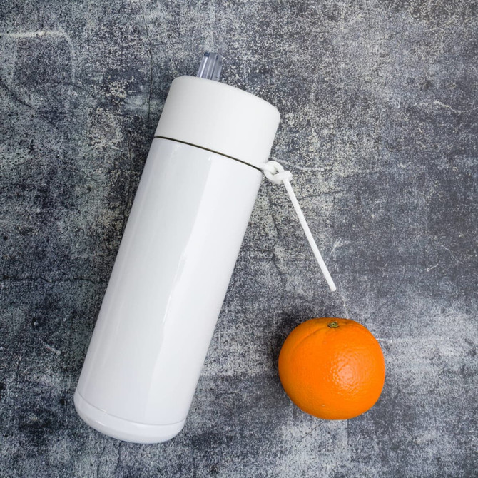 A drink bottle in white stainless steel with a clear straw attachment, placed next to an orange.