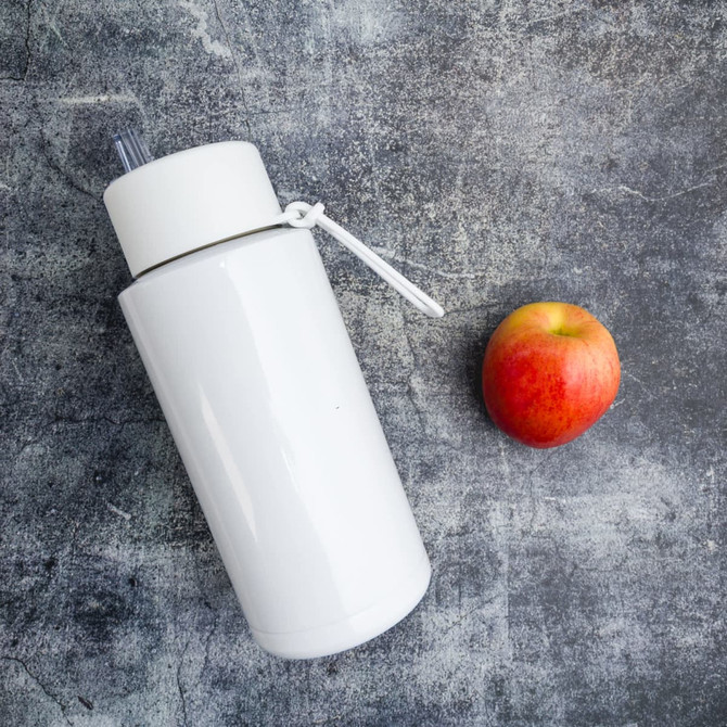 A drink bottle in white with a straw, positioned next to a red apple on a textured grey surface.
