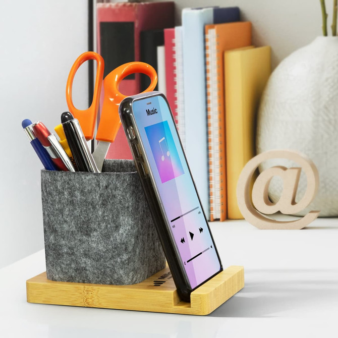 A bamboo phone stand desk caddy with grey felt storage, holding pens and scissors, alongside a smartphone.