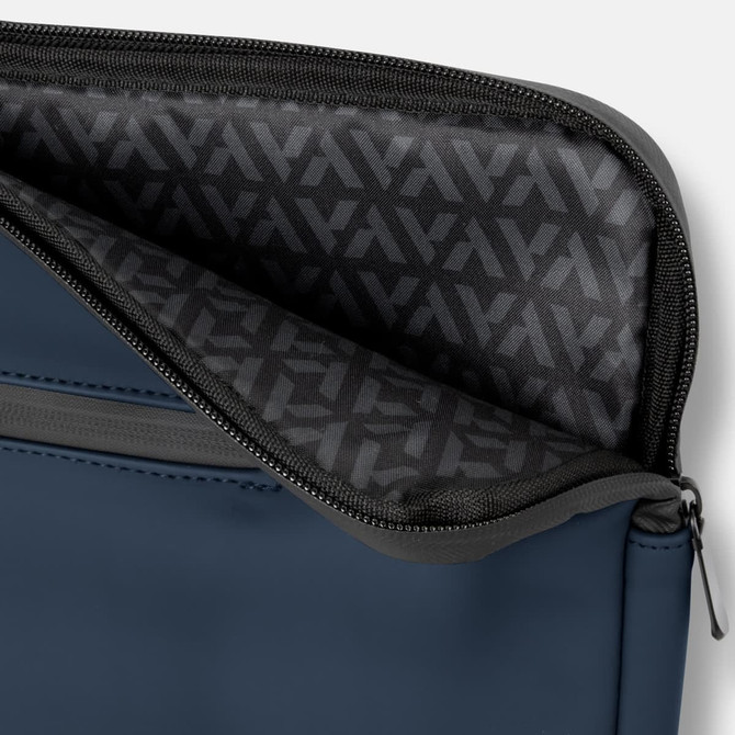 A navy soft-touch laptop sleeve features a grey zipper and a patterned interior lining. It includes branding.