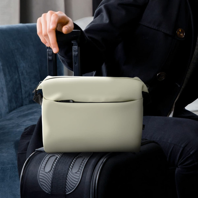A soft-touch toiletry bag in light cream, positioned on a suitcase, with two handles visible.