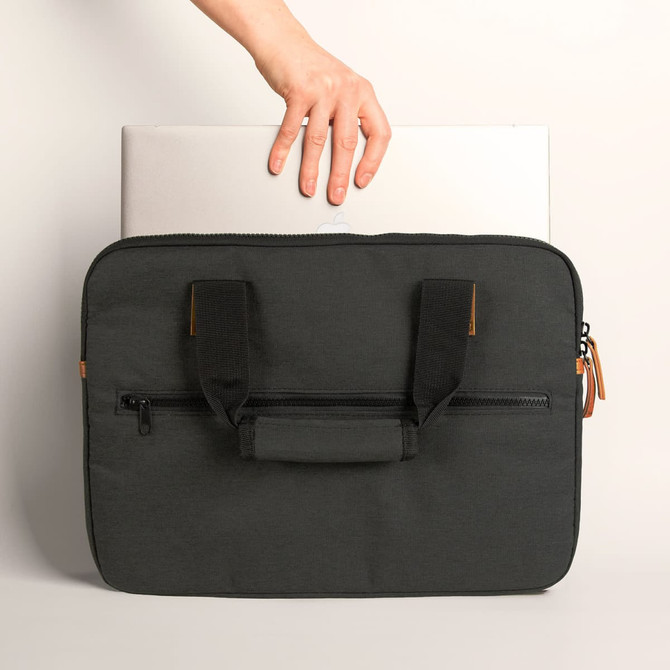 A black laptop bag with handles, featuring a zippered compartment, being held above a laptop.