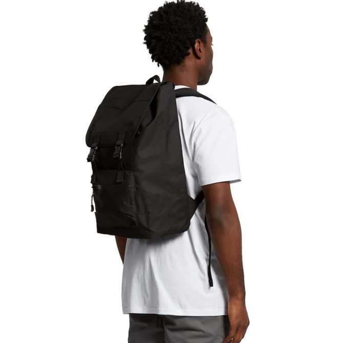 A black recycled field backpack worn over a person's shoulder, featuring adjustable straps and a simple design.