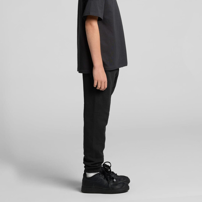 Black youth track pants displayed on a person, paired with a matching dark shirt and black shoes. Features a logo.