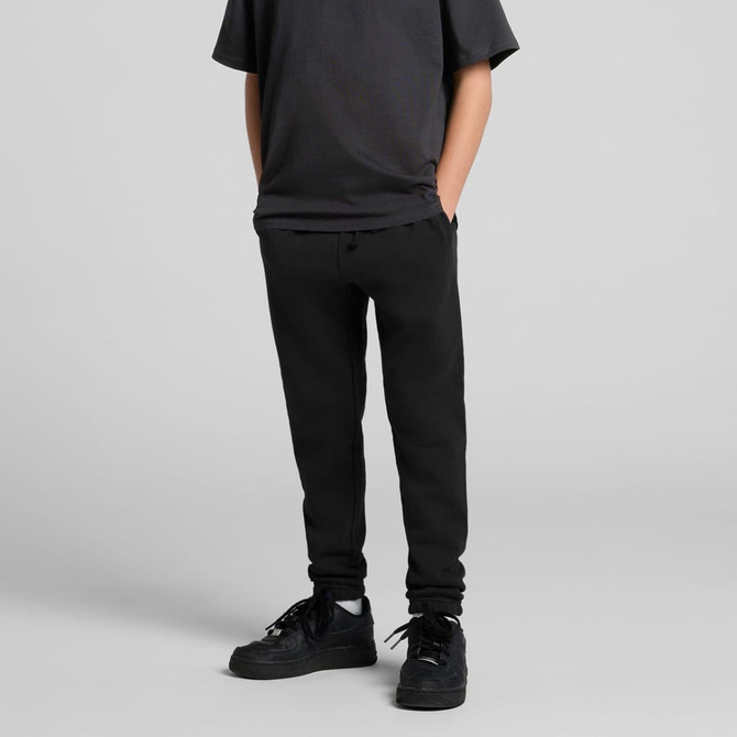 Black youth track pants featuring a fitted style and side pockets, worn with a black t-shirt and sneakers.