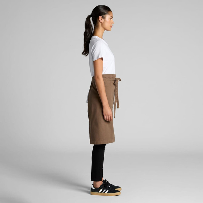 A brown canvas half apron is worn by a person in a white shirt and black pants, featuring a tied waist.