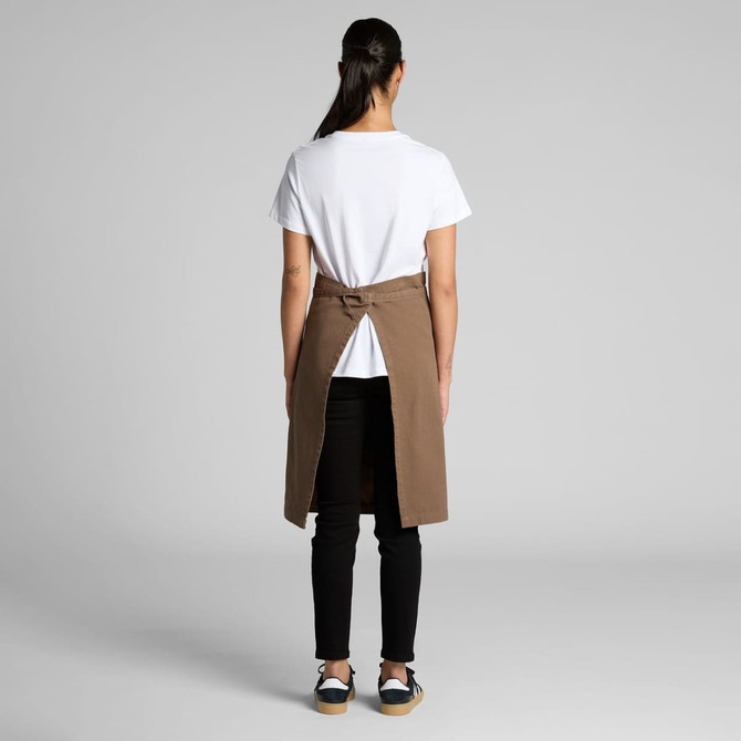 A brown canvas half apron with a tie waist, worn over a white t-shirt and black pants, featuring a back opening.