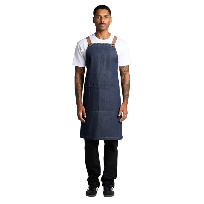 A denim apron featuring tan straps, worn by a person standing upright against a white background.