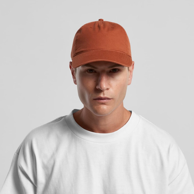 A five-panel cap in a rust colour, featuring a logo on the front, worn by a person in a white t-shirt.