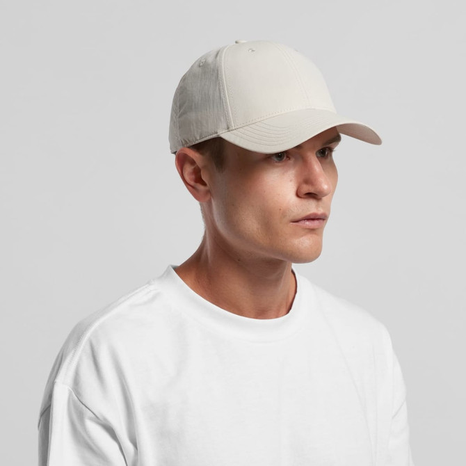 A beige nylon cap with a curved brim, worn by a model in a white t-shirt, featuring a logo on the front.