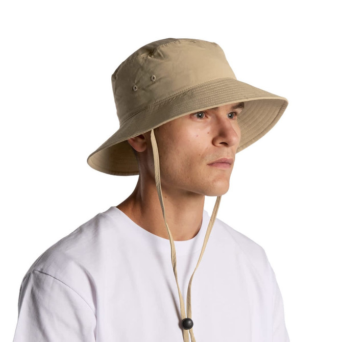 A beige nylon wide brim bucket hat with a chin strap, featuring ventilation eyelets and a logo.