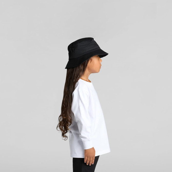 A child in a white long-sleeve tee and a black bucket hat, standing in profile against a neutral background.