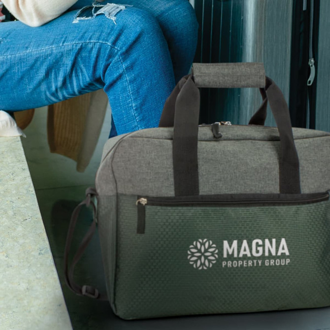 A grey and green business satchel with handles and a logo, resting beside a seated person in blue jeans.