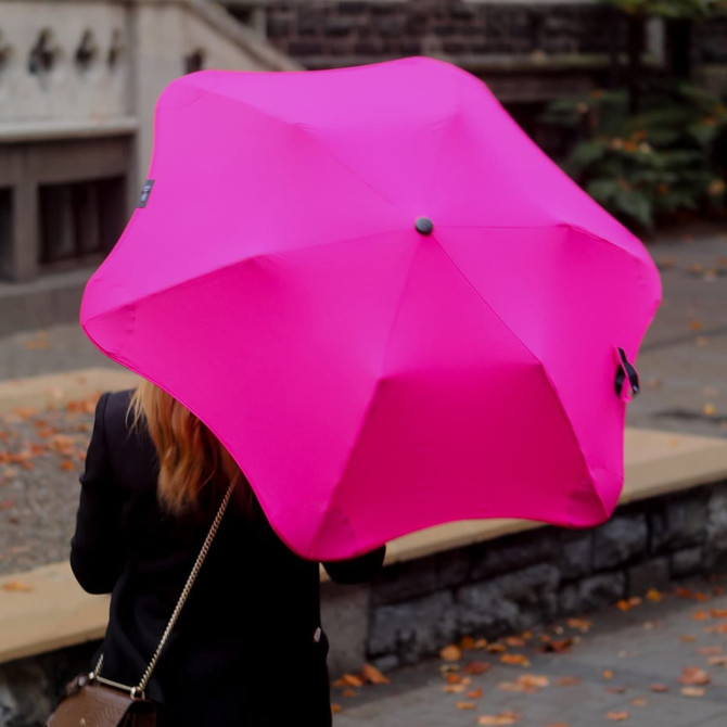 A pink BLUNT Metro Umbrella is being held by a person, showcasing its unique star-shaped design.