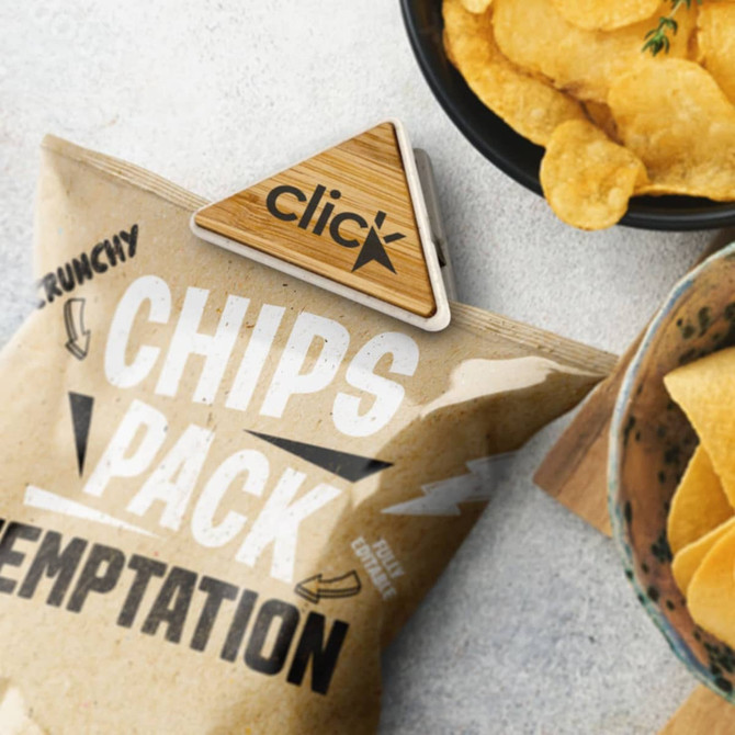 A bamboo handy clip secures a bag of chips, surrounded by crispy snacks on a textured surface.