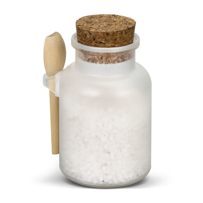A frosted glass jar filled with white bath salts, topped with a cork lid and a small wooden spoon.