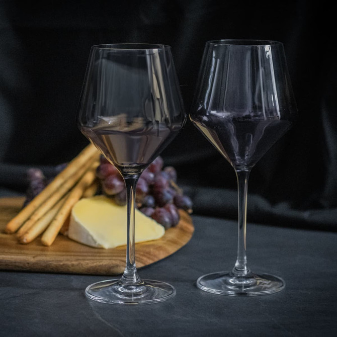 A set of two elegant dark purple wine glasses, accompanied by breadsticks, cheese, and grapes on a wooden platter.