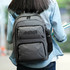 A grey backpack with a side mesh pocket for a drink bottle, carried by a person holding books.