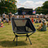 A black folding chair with a mesh backrest set against a vibrant outdoor festival scene.