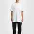 A white essential T-shirt, with short sleeves, displayed on a model, paired with black trousers. The shirt has a branding logo.