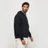 A black hoodie with a front pocket and a hood, displayed on a model standing sideways. Includes a logo.