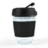A reusable coffee cup with a transparent body and a black flip lid. The cup features a black silicone sleeve for grip.