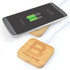 A bamboo wireless charger with a smartphone on top, showing a charging battery icon and featuring a logo.