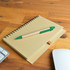 A brown spiral notebook placed on a wooden desk with a green pen resting on top and a computer mouse nearby.