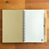 A recycled kraft notebook with lined pages, paired with a beige eco-friendly pen, featuring a logo.