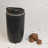 A reusable black coffee cup with a lid, placed next to several brown chocolate pieces on a speckled surface.