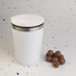 A white reusable coffee cup with a silver band at the top, alongside some brown candies.