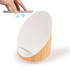 A wireless charger and speaker with a white top and bamboo base. A smartphone is held above the charger.