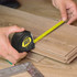 A tape measure with a black casing and yellow measuring tape is being used to measure wooden planks.
