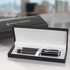 A sleek black pen with silver accents inside a black presentation box, featuring a logo on the lid.