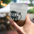 A plastic cup in a hand, featuring a frosted design and black branding, filled with a beverage.