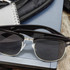 Maverick Sunglasses with a sleek black frame and dark lenses, placed on a surface with a notebook and backpack.