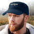 A navy Scout Military Style Cap with a bill is featured on a man with a beard, set against a natural background.