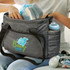 A grey baby bag with a logo, featuring compartments for bottles and diapers, being packed by a person.