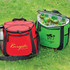 A red cooler bag and a green cooler bag, both filled with drink bottles, set on grass. Each bag has a logo.