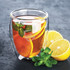 A double wall glass filled with tea, garnished with orange slices and mint leaves, beside fresh lemon. Features branding.