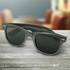 Carbon fibre sunglasses in grey, with dark lenses and a sleek design, displayed on a wooden surface.