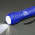 A blue torch with a textured grip and a strap, featuring a logo. It emits a bright white light.
