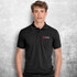 A black polo shirt on a model, featuring a logo on the left side. The shirt has a collared design and short sleeves.
