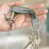 A grey and green reflector key ring with a carabiner, holding multiple keys, in a person’s hand.