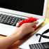 A red stress putty being squeezed in a hand, placed beside a laptop, notebook, sunglasses, and a calculator.