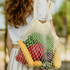 A cotton mesh tote bag in natural colour, filled with various fruits and vegetables, held by a person.