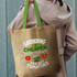 A jute tote bag with green handles, featuring a statement about gardening and tomatoes. It has a logo.